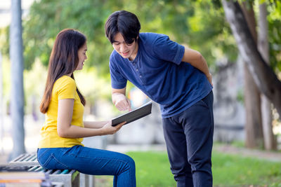 When sitting on a park bench, a pretty smiling young asian woman looks at her boyfriend's book.