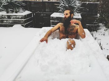 High angle view of shirtless bearded mid adult man sitting in snow covered container