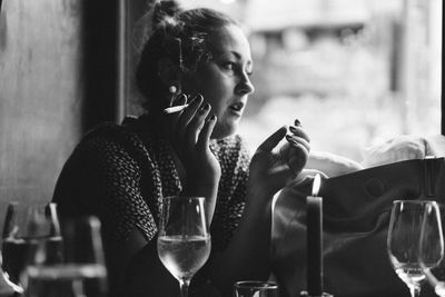 Side view of woman smoking cigarette while sitting with wineglass at restaurant table