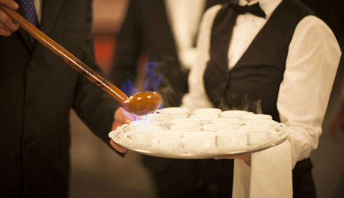 Midsection of man pouring flaming drinks into cups