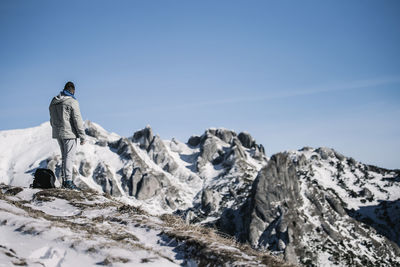 Rear view of man standing on mountain peak against sky during winter
