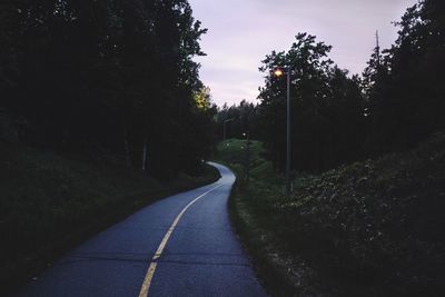 Empty road along trees and plants against sky