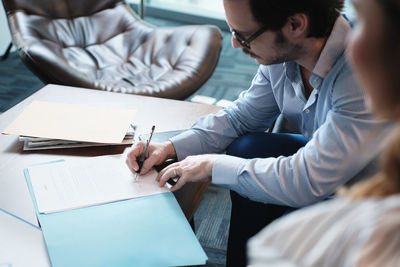High angle view of businessman signing document while sitting with coworker in office
