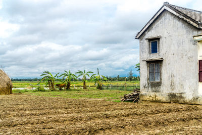 Barn on field by house against sky