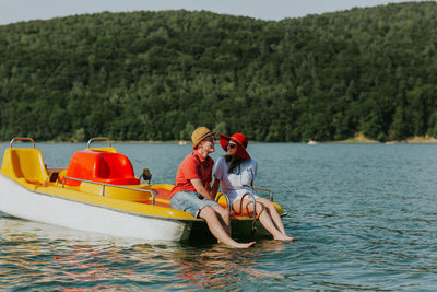 Cheerful man and woman in paddleboat on lake against sky