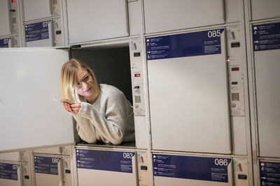 Young woman holding mobile phone in locker