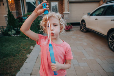 Close-up of girl blowing bubbles while standing against house