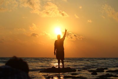 Silhouette man standing on beach against sky during sunset