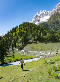 Rear view of man walking on mountain against clear blue sky