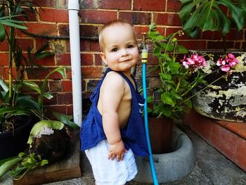 Portrait of cute baby boy standing by potted plant and faucet