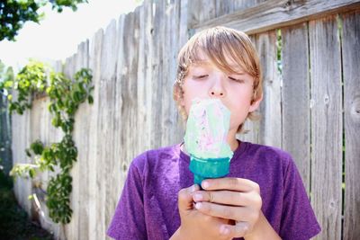 Close-up of boy enjoying ice cream against wooden fence