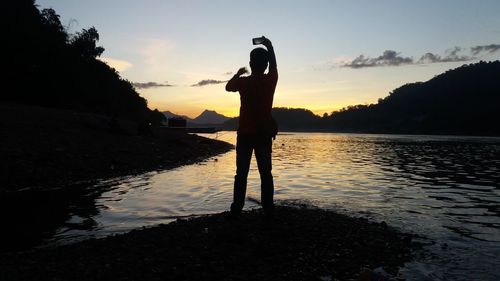 Silhouette man standing by lake against sky during sunset