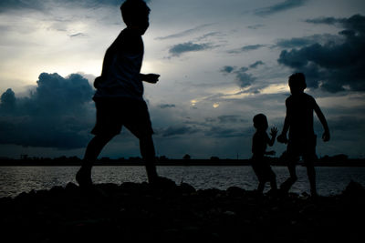 Silhouette people on beach against sky during sunset