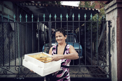 Portrait of woman selling food while standing against gate