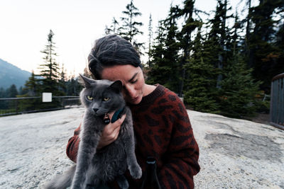 Young woman enjoys a time in wilderness holding and loving on her cat