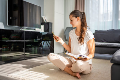 Side view of young woman using mobile phone while sitting at home