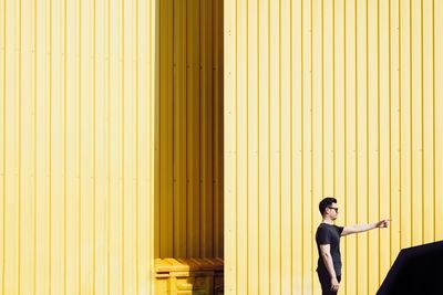 Side view of mid adult man pointing while standing against yellow wall