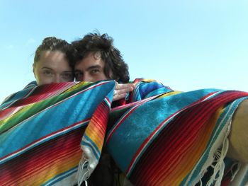 Couple covered with blanket against sky