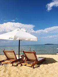 Lounge chairs with parasol at beach against sky