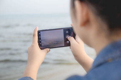 Midsection of man photographing with mobile phone in sea