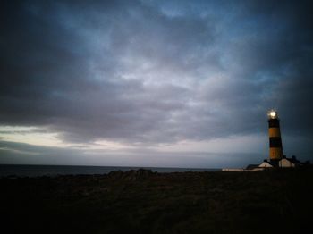 Lighthouse by sea against sky during sunset