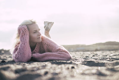 Woman lying on sand at beach against sky