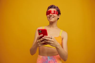 Portrait of young woman using mobile phone against yellow background