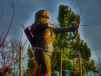 Rear view of woman standing by tree against sky