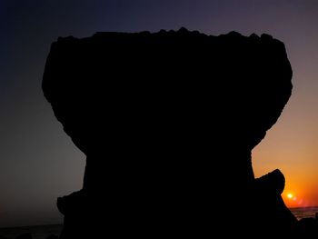 Close-up of silhouette people standing on rock against sky during sunset