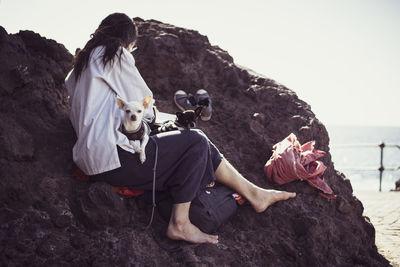 Natural woman sits on rock with two cute dogs on lap by ocean in spain