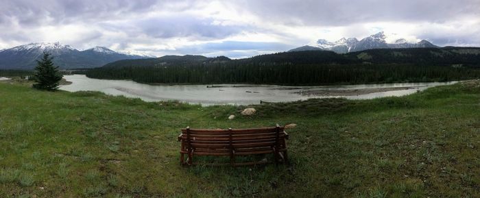 Empty benches on field by mountains against sky