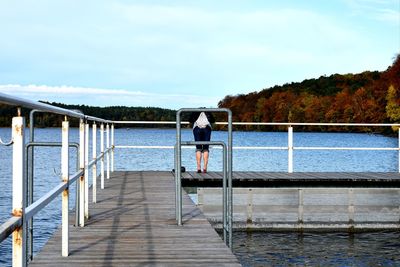 Rear view of man standing on pier by sea against sky