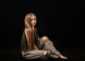 Full length of woman sitting against black background