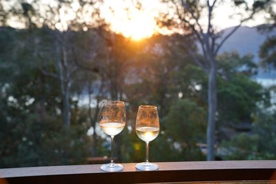 Wine glass on table against trees during sunset