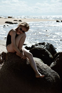 Full length of young woman sitting on rock at beach