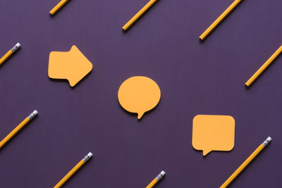 Close-up of yellow pencils and speech bubbles on purple table