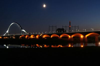 Illuminated bridge over river against sky at night