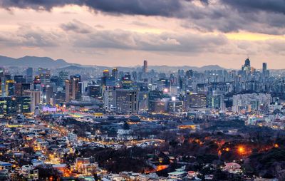 High angle view of illuminated city buildings against sky during sunset