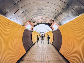 Rear view of people walking on footpath in tunnel