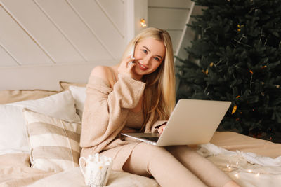 A beautiful blonde young woman in a knitted sweater celebrates the christmas holiday at home