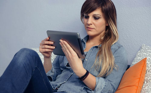 Woman using digital tablet while leaning on bed at home