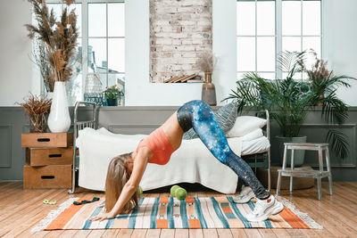 Beautiful young woman exercising in the bedroom, downward facing dog pose. 