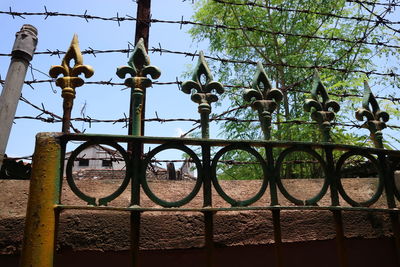 Trees seen through fence against sky