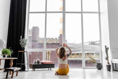 Rear view of woman sitting by glass window at home