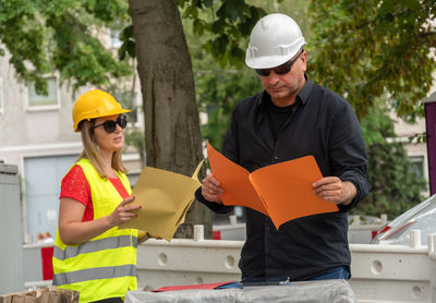 Colleagues wearing hardhat while reading paperwork on construction site