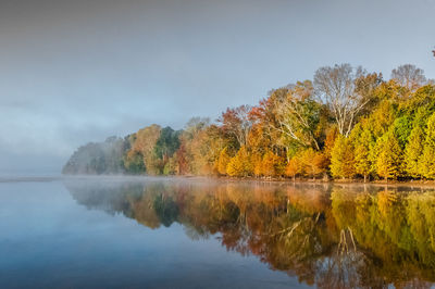 Trees by lake against sky during autumn