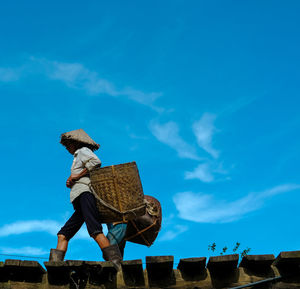 Men carrying wicker basket walking on bridge against sky