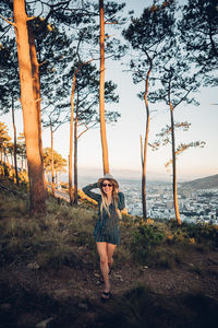 Full length of young woman standing by tree against sea