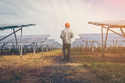 Rear view of man walking by solar panels on field against sky