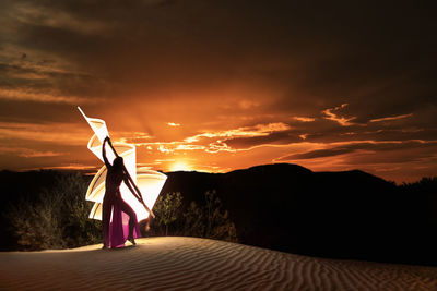 Silhouette woman standing on street against sky during sunset